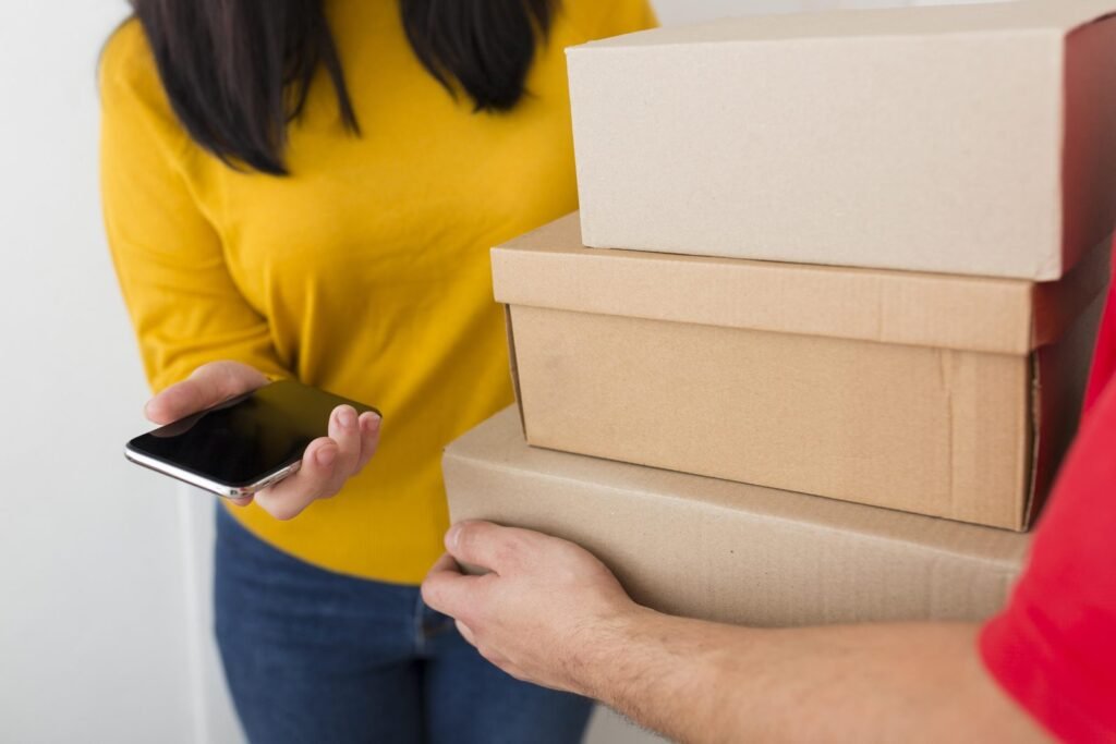 Persona con un teléfono celular en la mano recibe cajas de un pedido