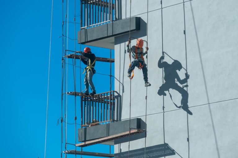 Dos trabajadores con casco y arnés trabajan en un andamio de obra